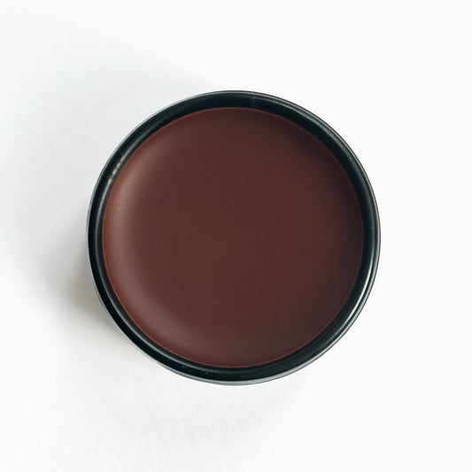 An open black aluminum tin of Nuska Cocoa Natural Tinted Lip Balm, showing the creamy texture and colour of the moisturizing balm.