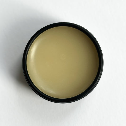 An open black aluminum tin of Nuska Coconut Natural Lip Balm, showing the creamy texture and natural color of the moisturizing balm.