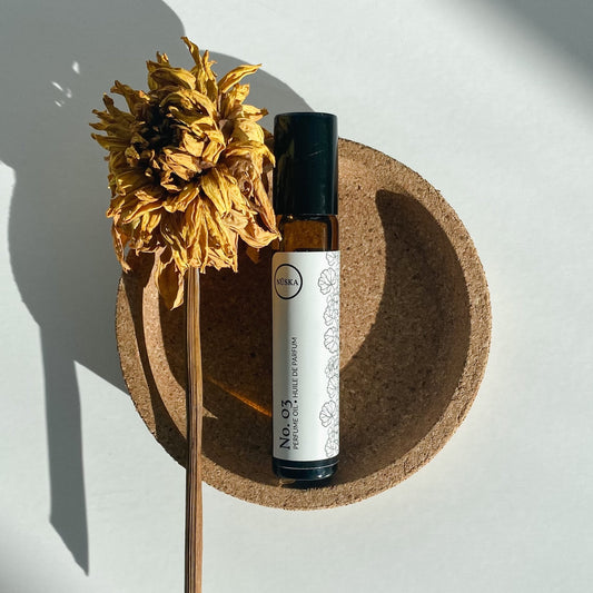 Nuska Botanical Perfume Oil No.3 in a roll-on amber glass bottle, surrounded by natural light and a dried yellow flower, highlighting its fougere, fresh, herbal, and woody scent from essential oils.
