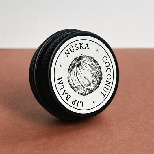 A black aluminum tin with a gray label of Nuska coconut natural lip balm.