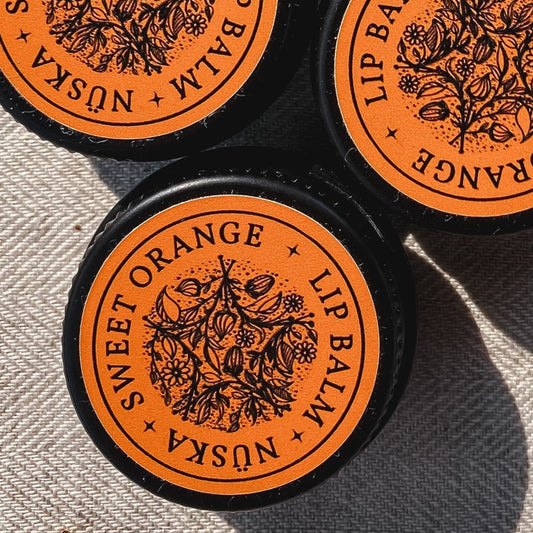 A black aluminum tin with an orange label of Nuska sweet orange natural lip balm.