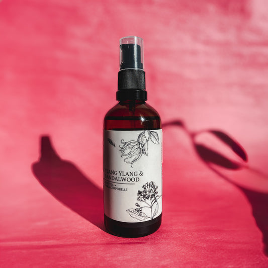 An amber glass pump bottle of 100 ml of Nuska Ylang Ylang & Sandalwood Botanical body oil with a pink background.