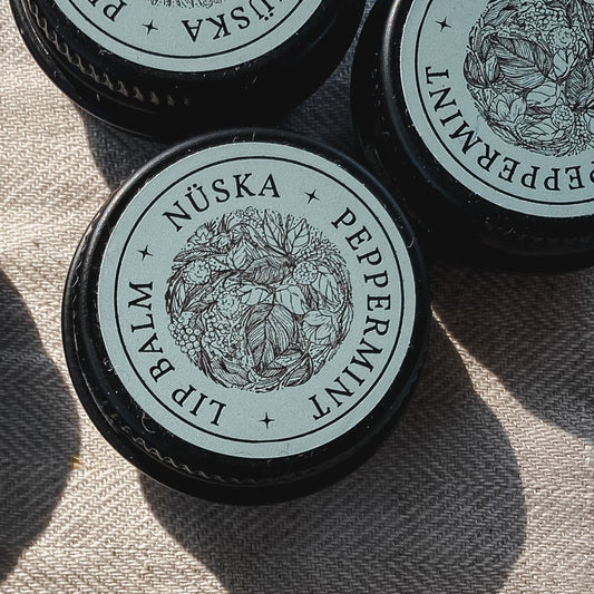 A black aluminum tin with a sage green label of Nuska peppermint natural lip balm.